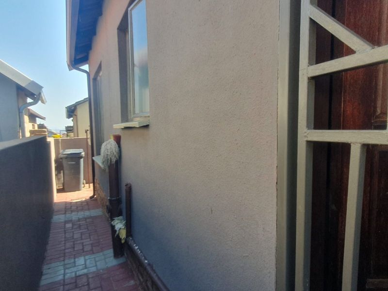 A side exterior walkway featuring paved flooring, a security gate, and a plastered wall with a window.
