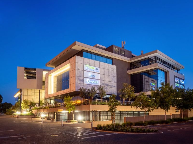 Modern commercial office building featuring a contemporary concrete and glass facade, integrated parking entrance, and professional exterior lighting at dusk.