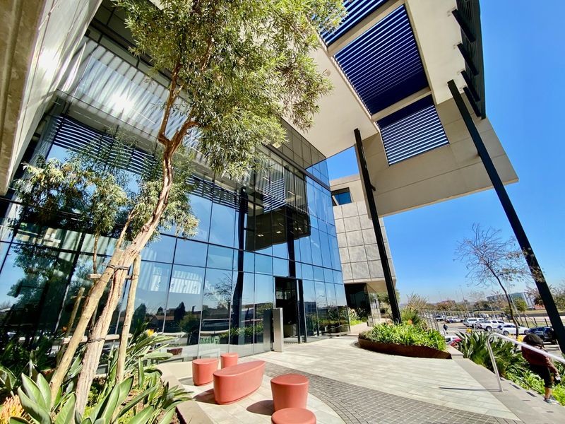 Modern commercial building entrance featuring a striking glass facade, expansive louvred canopy, and well-maintained landscaped surroundings.