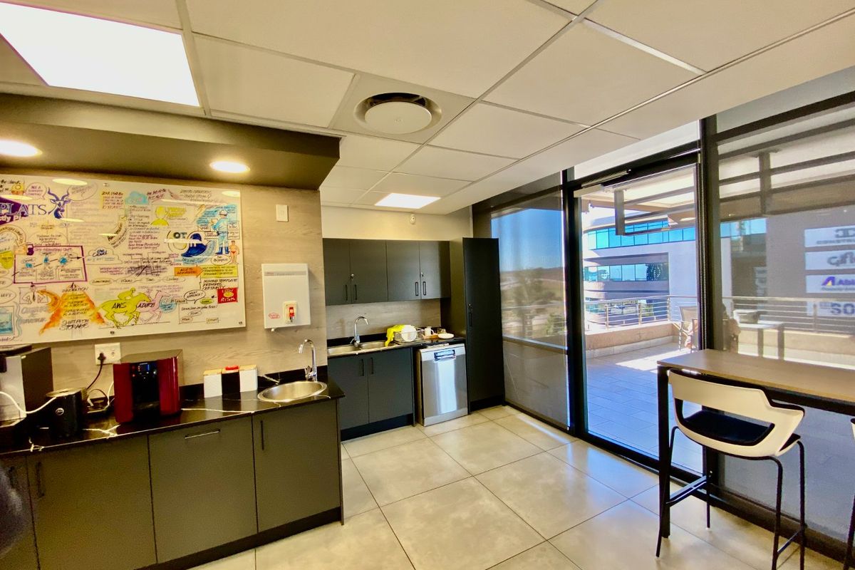 Modern commercial kitchenette featuring dark cabinetry, integrated sink, dishwasher, and tiled flooring, with direct access to an outdoor balcony area.