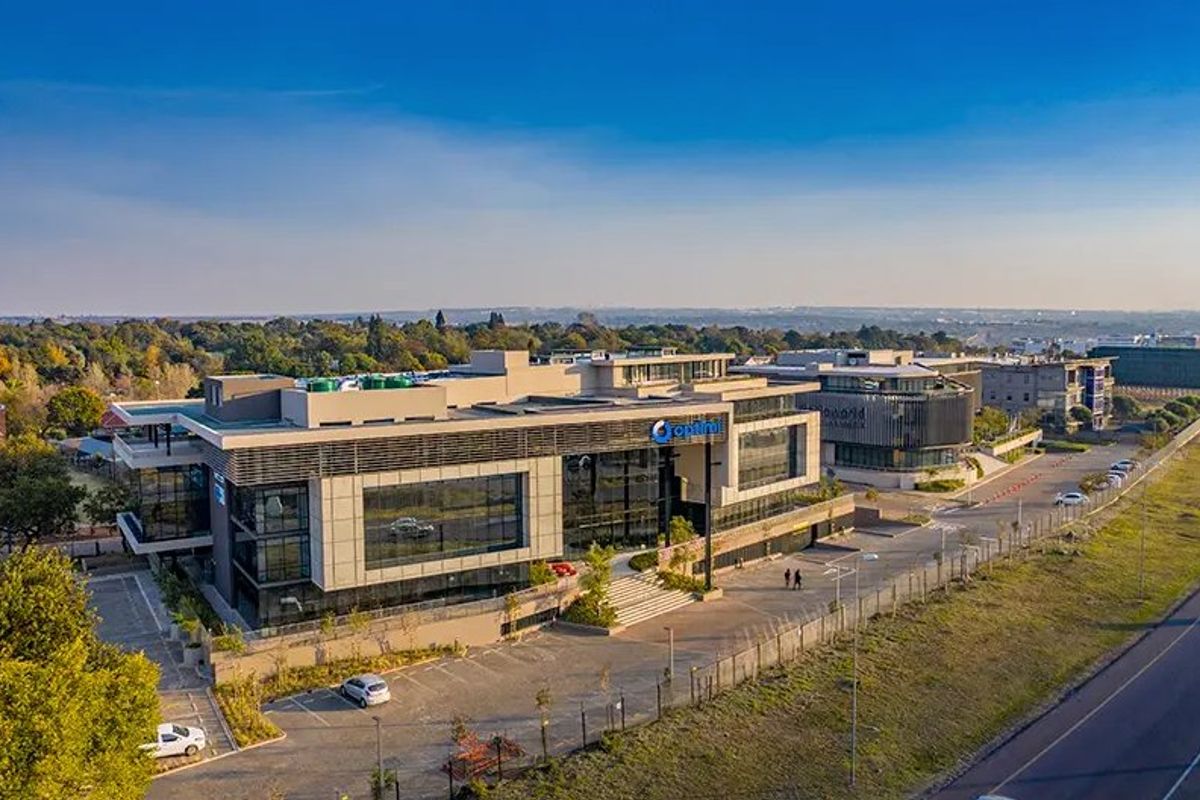 Aerial view of a modern multi-story commercial office building featuring glass facades, extensive parking facilities, and landscaped surroundings in a business park setting.