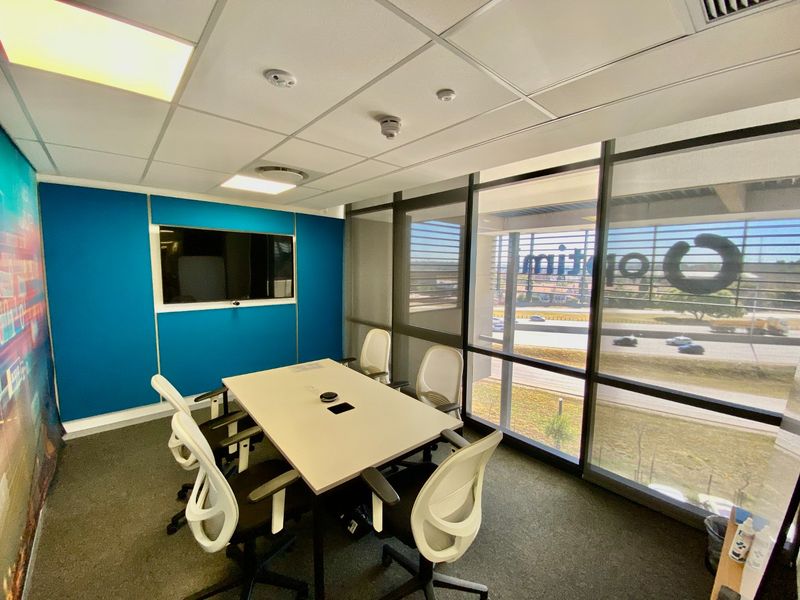 A modern, well-lit office meeting room featuring floor-to-ceiling windows, carpeted flooring, and a professional suspended ceiling with integrated lighting.