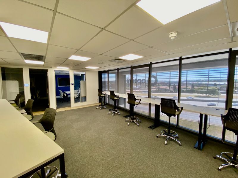 Modern commercial office space featuring a built-in window desk, suspended ceiling with recessed lighting, and large windows providing natural light and exterior views.