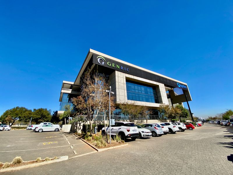 Modern commercial office building featuring a glass and concrete facade with dedicated paved parking and prominent corporate signage.