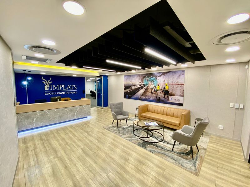 Modern commercial reception area featuring a marble-fronted desk, baffle ceiling design, recessed lighting, and high-quality laminate flooring.