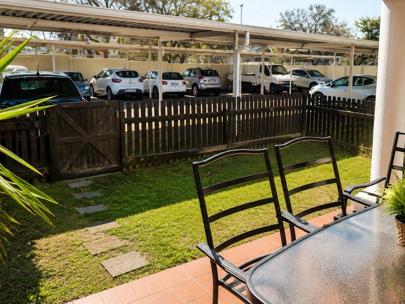 A private patio area featuring tiled flooring, a small lawn, and a wooden fence, overlooking the complex's covered parking area.