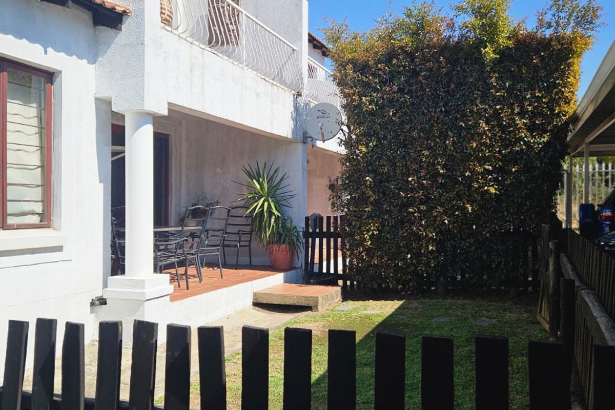 Rear view of the apartment featuring a covered patio, small garden area, and adjacent carport parking.