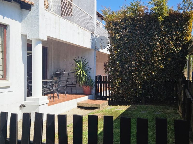 Rear view of the apartment featuring a covered patio, small garden area, and adjacent carport parking.