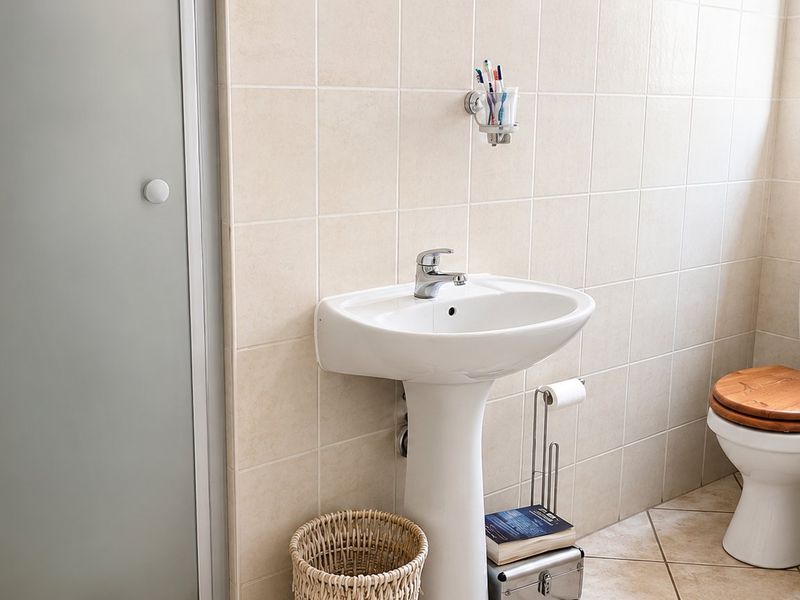 A functional bathroom featuring a pedestal basin, toilet, and bathtub with neutral ceramic wall and floor tiling.