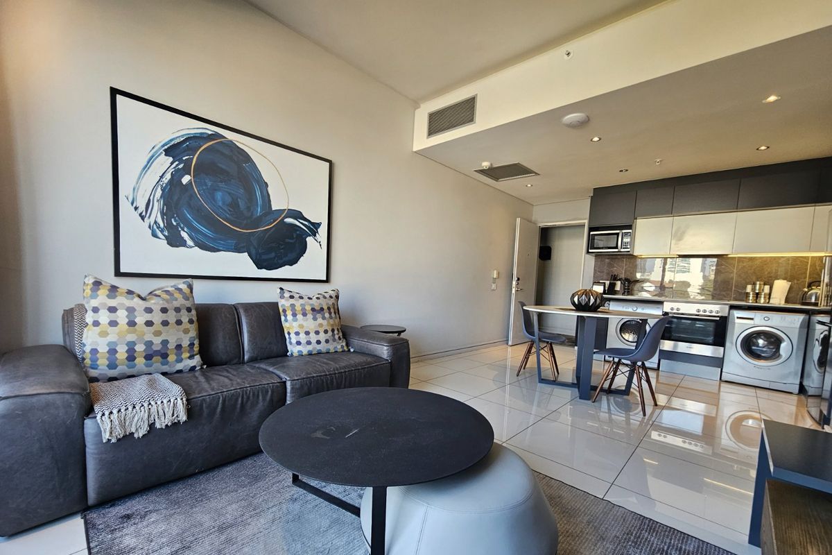 Modern open-plan living area featuring a sleek kitchen with integrated appliances, tiled flooring, and recessed lighting, creating a functional and contemporary apartment space.