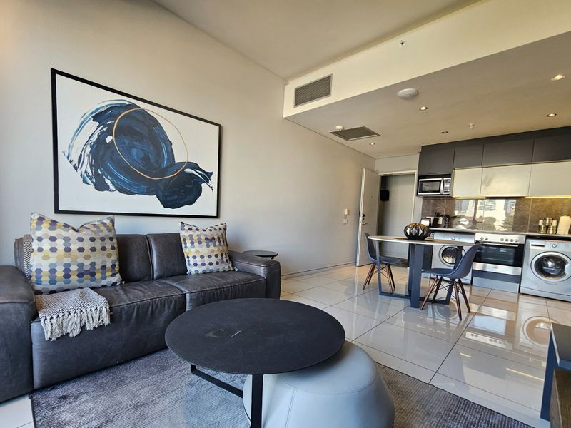 Modern open-plan living area featuring a sleek kitchen with integrated appliances, tiled flooring, and recessed lighting, creating a functional and contemporary apartment space.