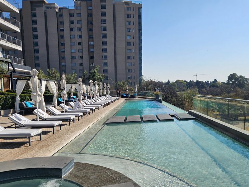 A well-maintained infinity pool area featuring timber decking, a glass balustrade, and a built-in spa, offering an elevated outdoor leisure space.