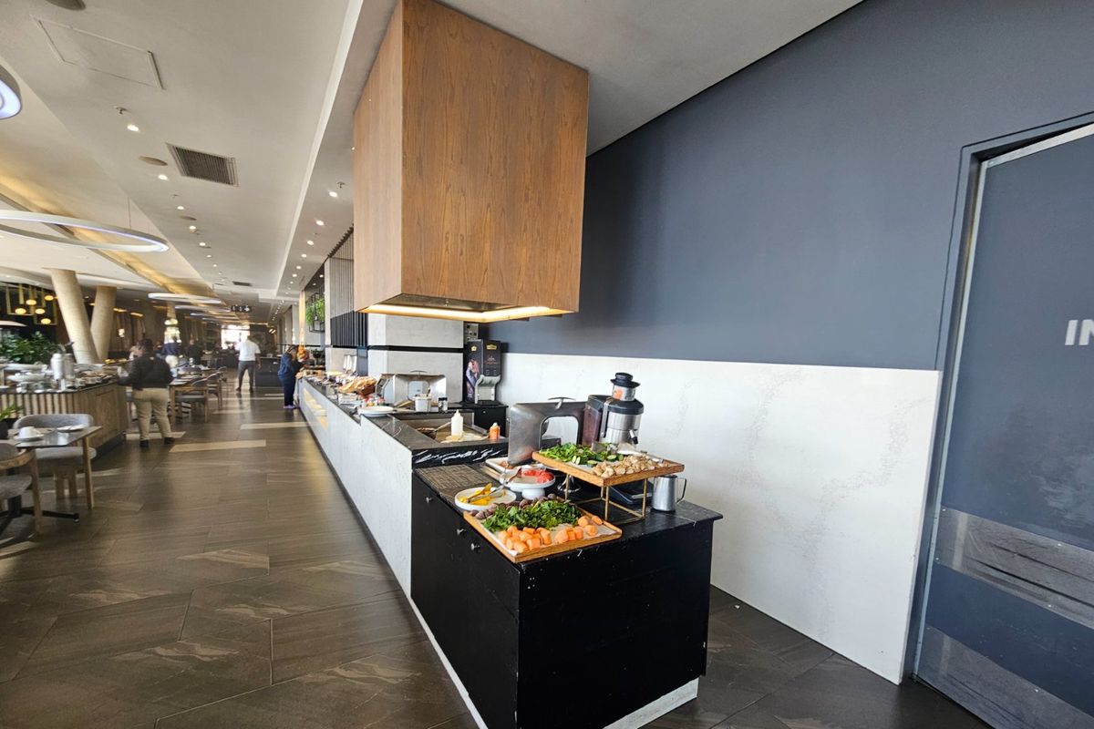 A modern commercial-style kitchen area featuring a prominent wooden extractor hood, stone countertops, and sleek tiled flooring in a contemporary setting.