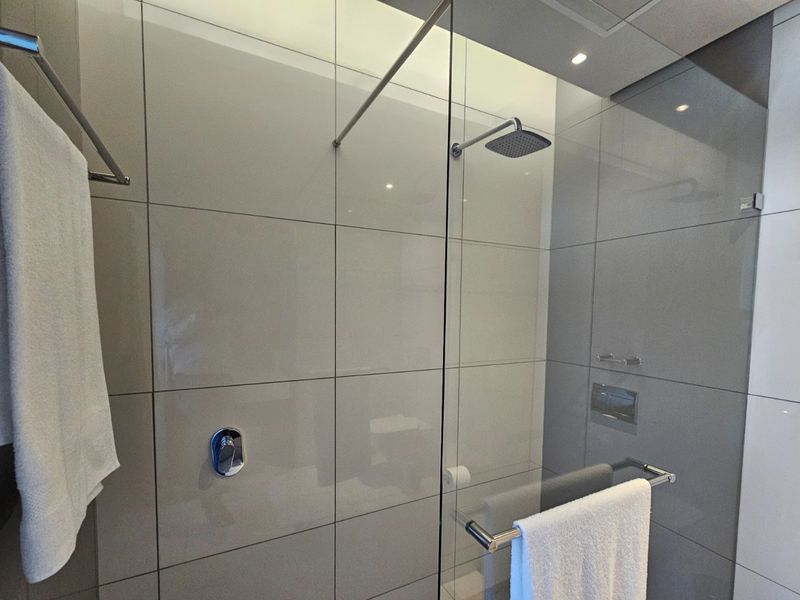 Modern bathroom shower enclosure featuring large-format grey ceramic wall tiles, a glass screen, and a contemporary rain shower head.