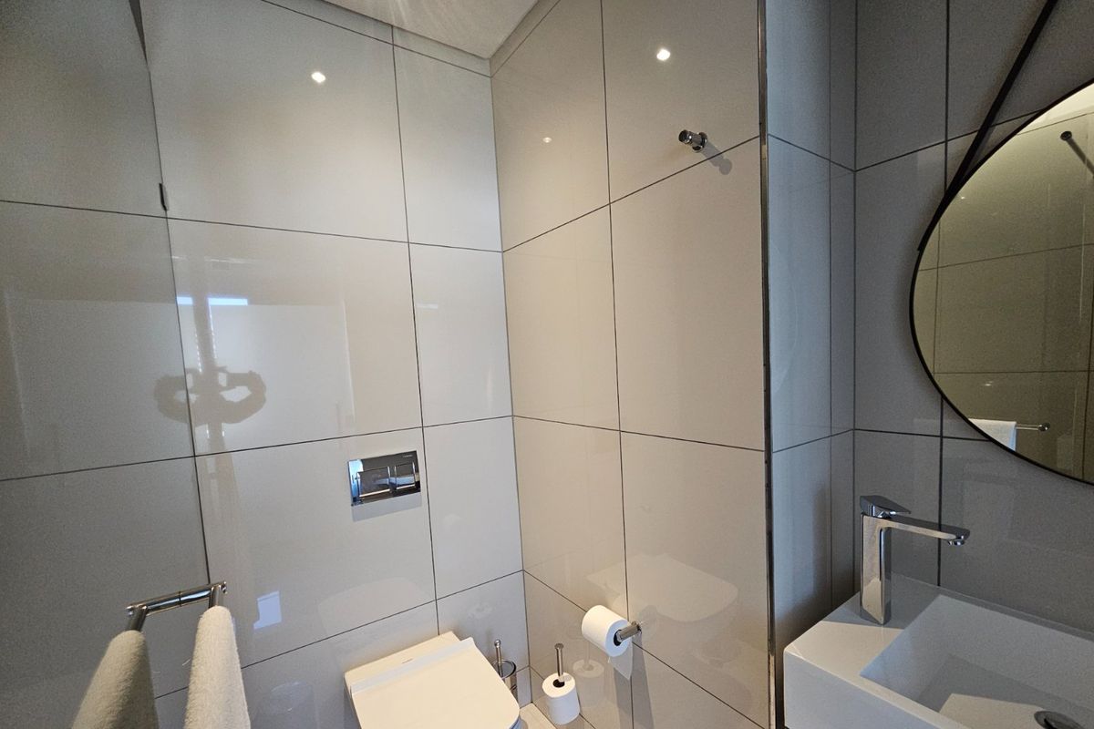 Modern bathroom featuring large format wall tiles, a wall-mounted toilet with chrome flush plate, and a sleek vanity basin with a chrome mixer tap.