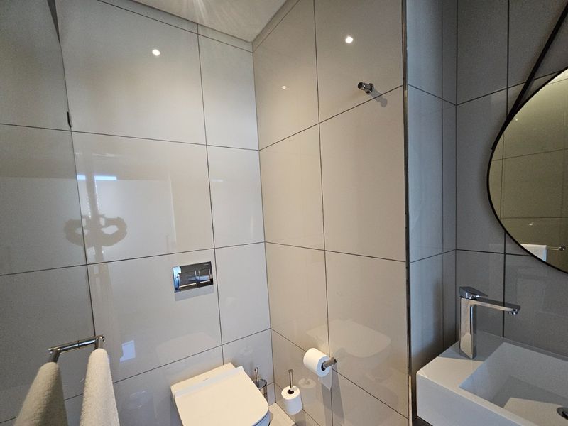 Modern bathroom featuring large format wall tiles, a wall-mounted toilet with chrome flush plate, and a sleek vanity basin with a chrome mixer tap.