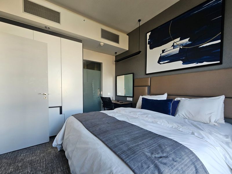Modern bedroom featuring a built-in wardrobe, integrated ducted air conditioning, and a stylish upholstered headboard with neutral finishes.