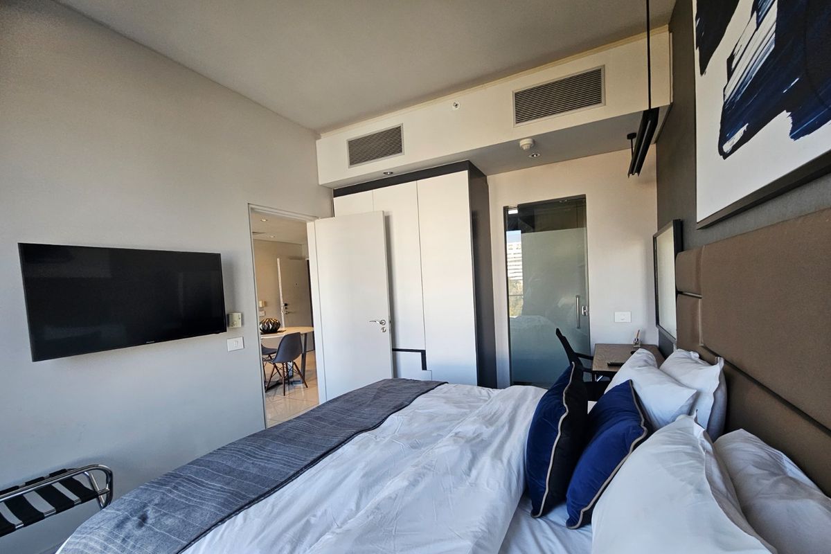 Modern bedroom featuring built-in cabinetry, ducted air conditioning, and a frosted glass door leading to an en-suite bathroom.