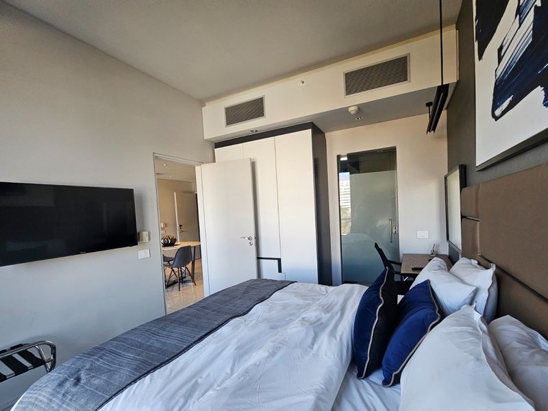 Modern bedroom featuring built-in cabinetry, ducted air conditioning, and a frosted glass door leading to an en-suite bathroom.