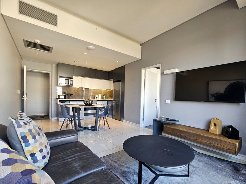 Modern open-plan living area featuring a sleek kitchen with built-in appliances, tiled flooring, and ducted air conditioning in a contemporary apartment setting.
