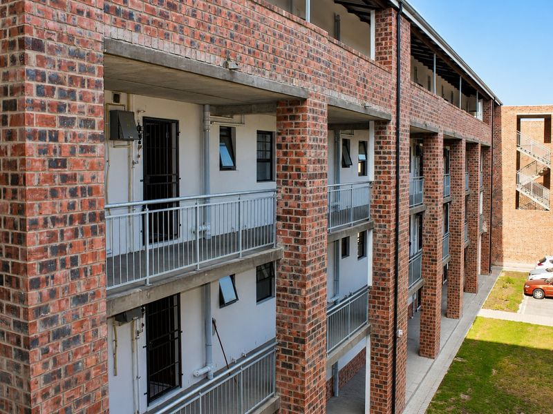 Exterior view of a multi-story apartment building featuring exposed brickwork, concrete balconies with metal railings, and secure access points.