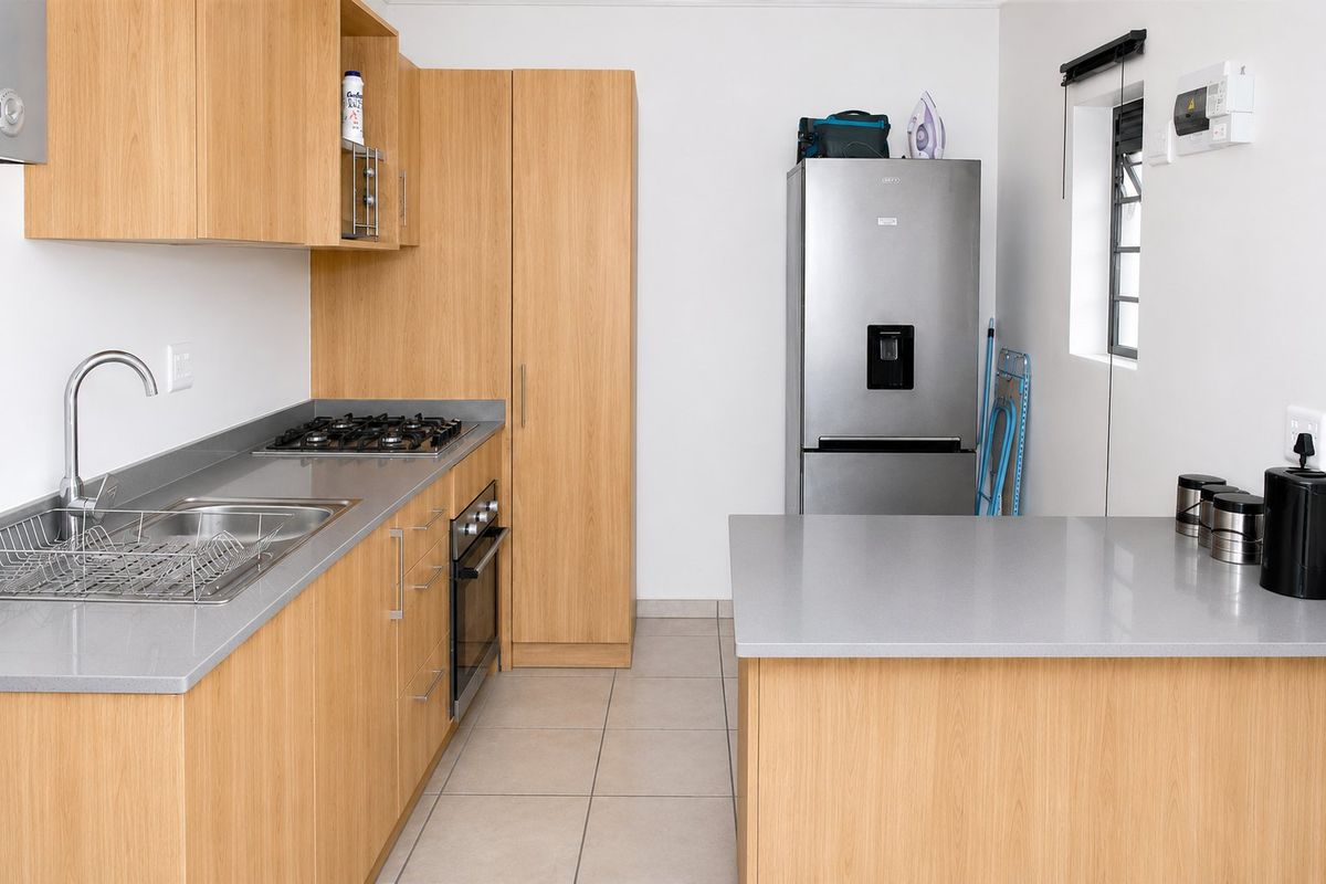 Modern kitchen featuring light wood cabinetry, stone countertops, a gas hob, built-in oven, and tiled flooring in a clean, functional layout.