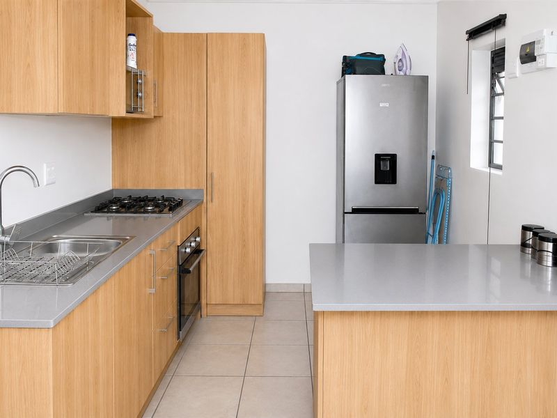 Modern kitchen featuring light wood cabinetry, stone countertops, a gas hob, built-in oven, and tiled flooring in a clean, functional layout.