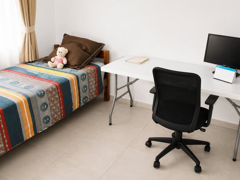 A functional bedroom featuring neutral tiled flooring and a window with installed curtain rods, providing a clean and simple living space.