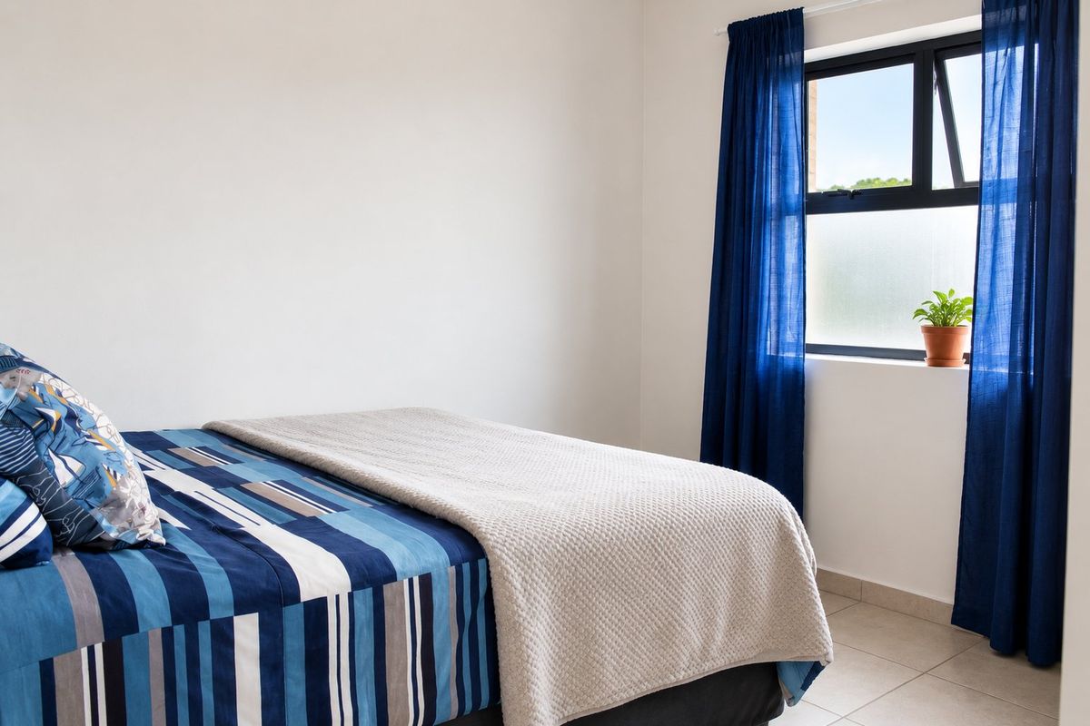 A bright and well-maintained bedroom featuring neutral tiled flooring and a modern aluminium window frame with natural light.