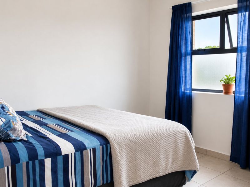 A bright and well-maintained bedroom featuring neutral tiled flooring and a modern aluminium window frame with natural light.