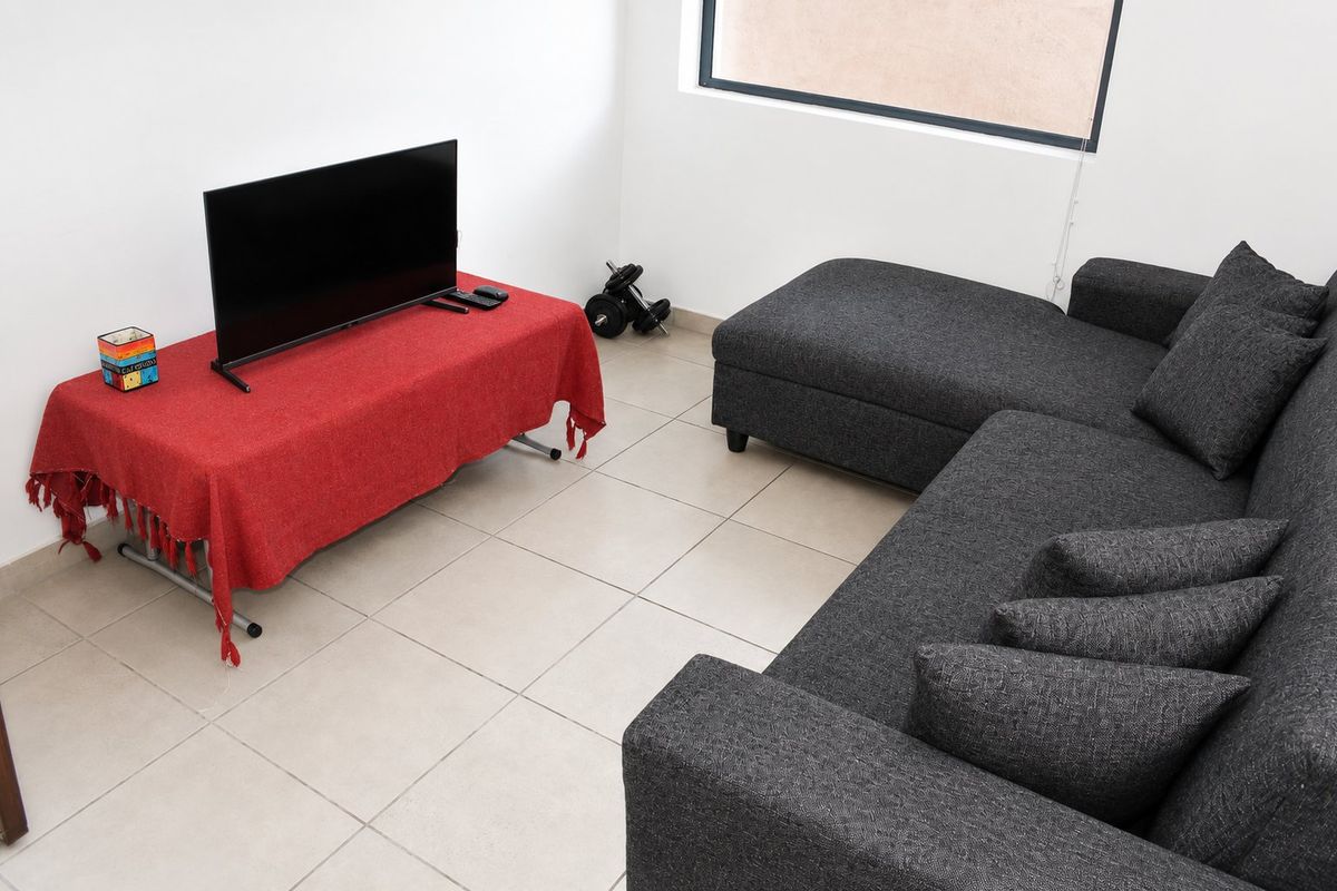 A functional living room area featuring neutral tiled flooring and a large window, providing a bright and simple space for relaxation.