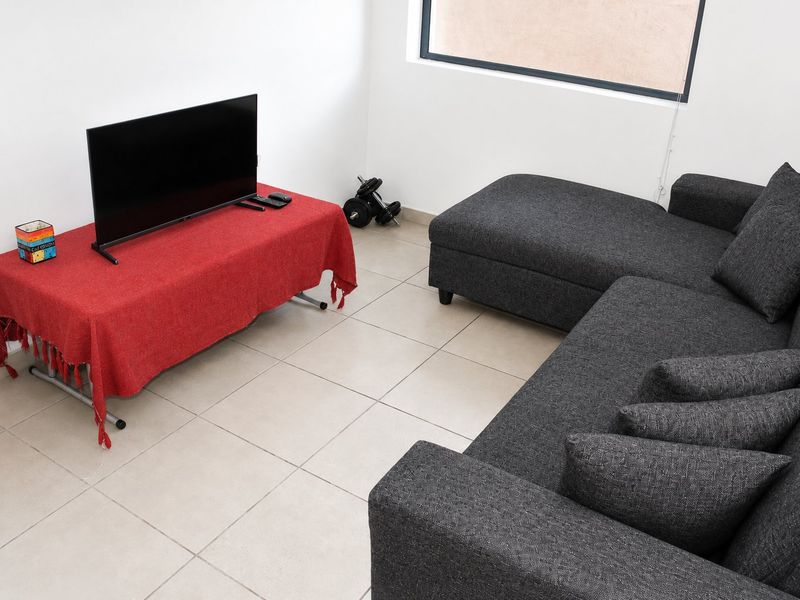 A functional living room area featuring neutral tiled flooring and a large window, providing a bright and simple space for relaxation.