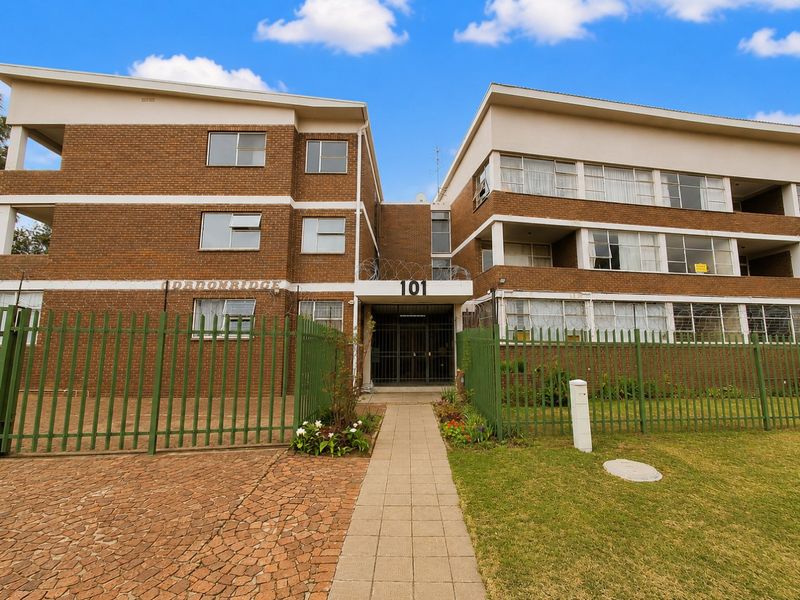 Front exterior view of the Dadonridge apartment complex, featuring a brick facade, secure gated entrance, and paved walkway leading to the main building access.