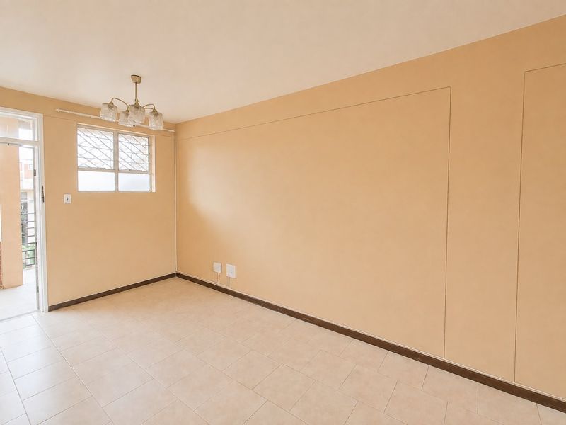An empty living room featuring neutral tiled flooring, a ceiling light fixture, and a window with security bars, offering a clean, blank canvas.
