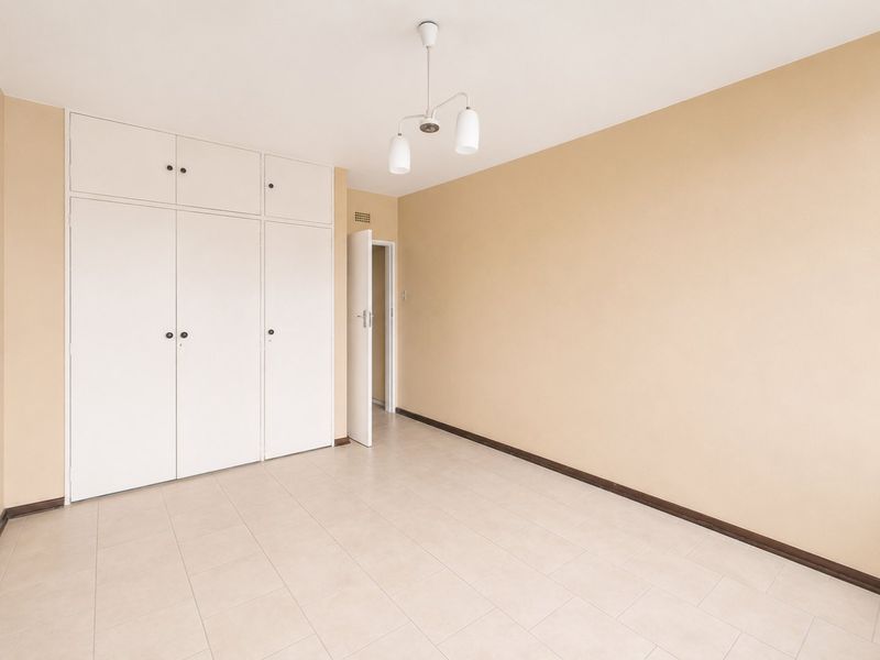 An empty bedroom featuring neutral wall paint, tiled flooring, and ample built-in cupboard storage space.