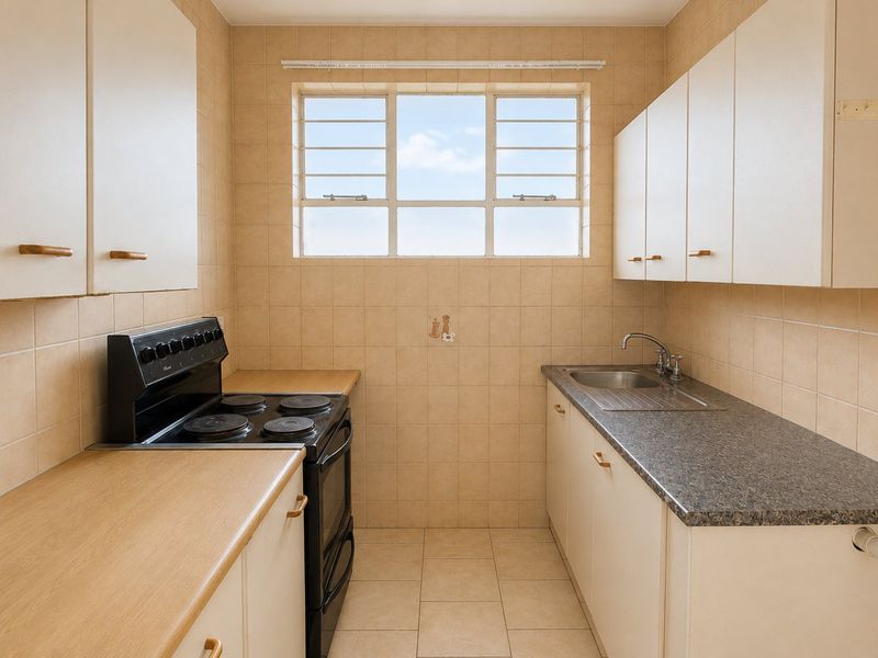 A functional galley-style kitchen featuring tiled walls, laminate countertops, built-in cabinetry, and a freestanding electric stove under a bright window.