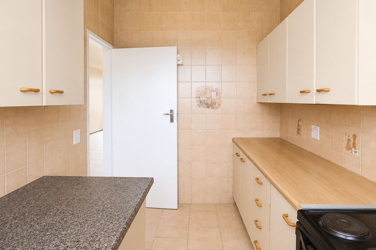 A functional kitchen featuring tiled walls and flooring, ample built-in cabinetry, laminate countertops, and a built-in electric stove.