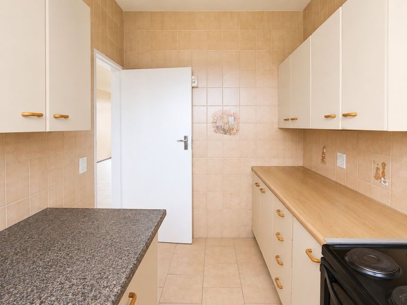 A functional kitchen featuring tiled walls and flooring, ample built-in cabinetry, laminate countertops, and a built-in electric stove.