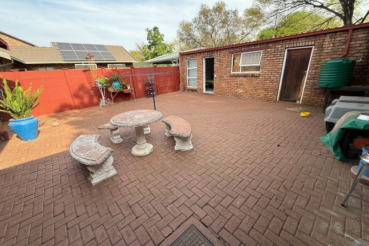 A paved rear courtyard area featuring a brick outbuilding, boundary wall, and solar panels installed on the main roof structure.