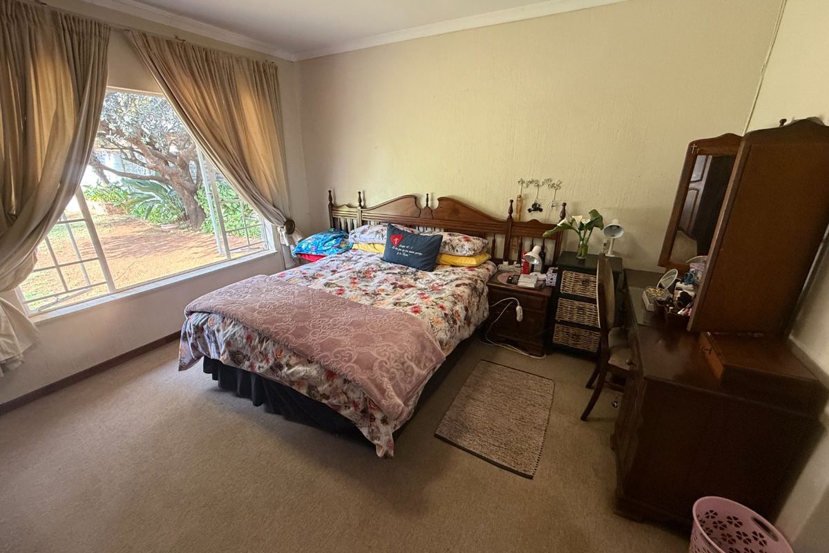 A standard bedroom featuring carpeted flooring, a large window with natural light, and classic cornice detailing.
