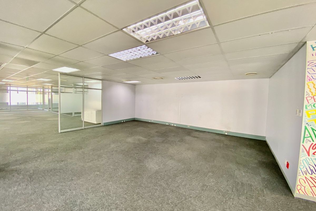 An empty commercial office space featuring a suspended ceiling with recessed lighting, glass partitioning, and carpeted flooring.