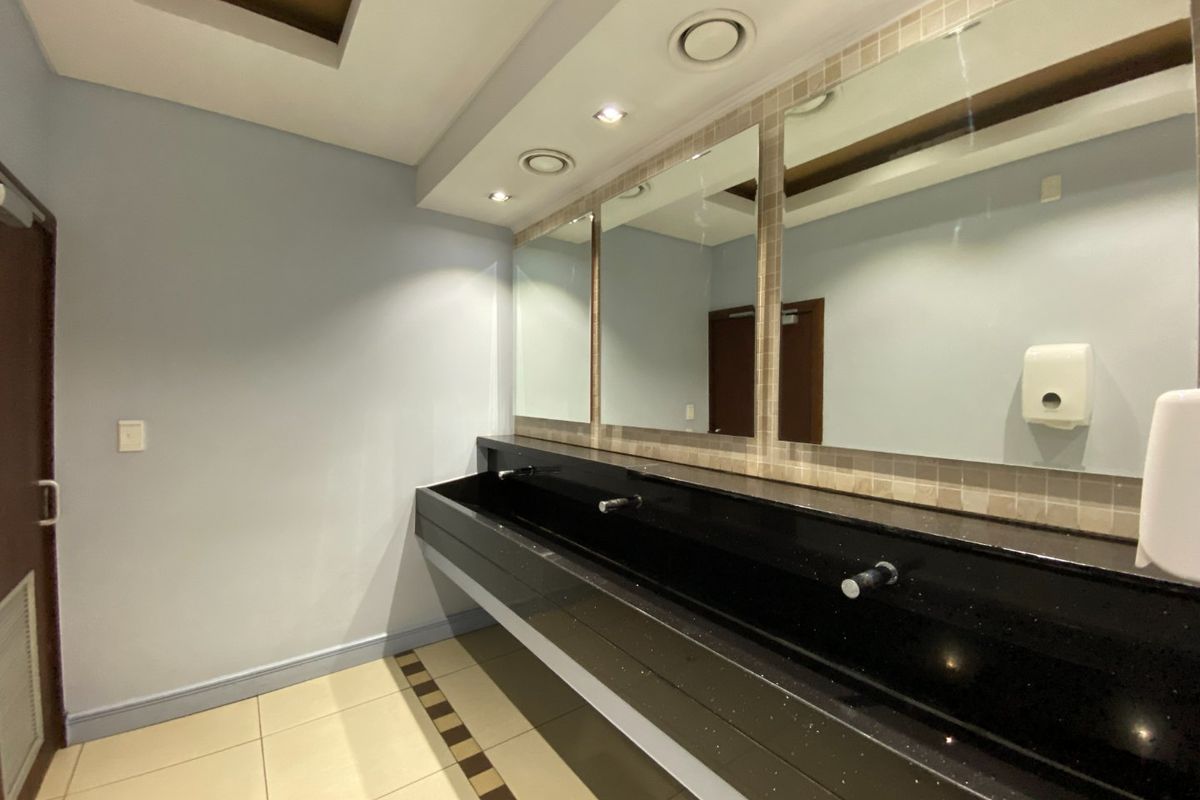 A clean, modern commercial bathroom featuring a long black stone vanity countertop with integrated basins and large wall-mounted mirrors.