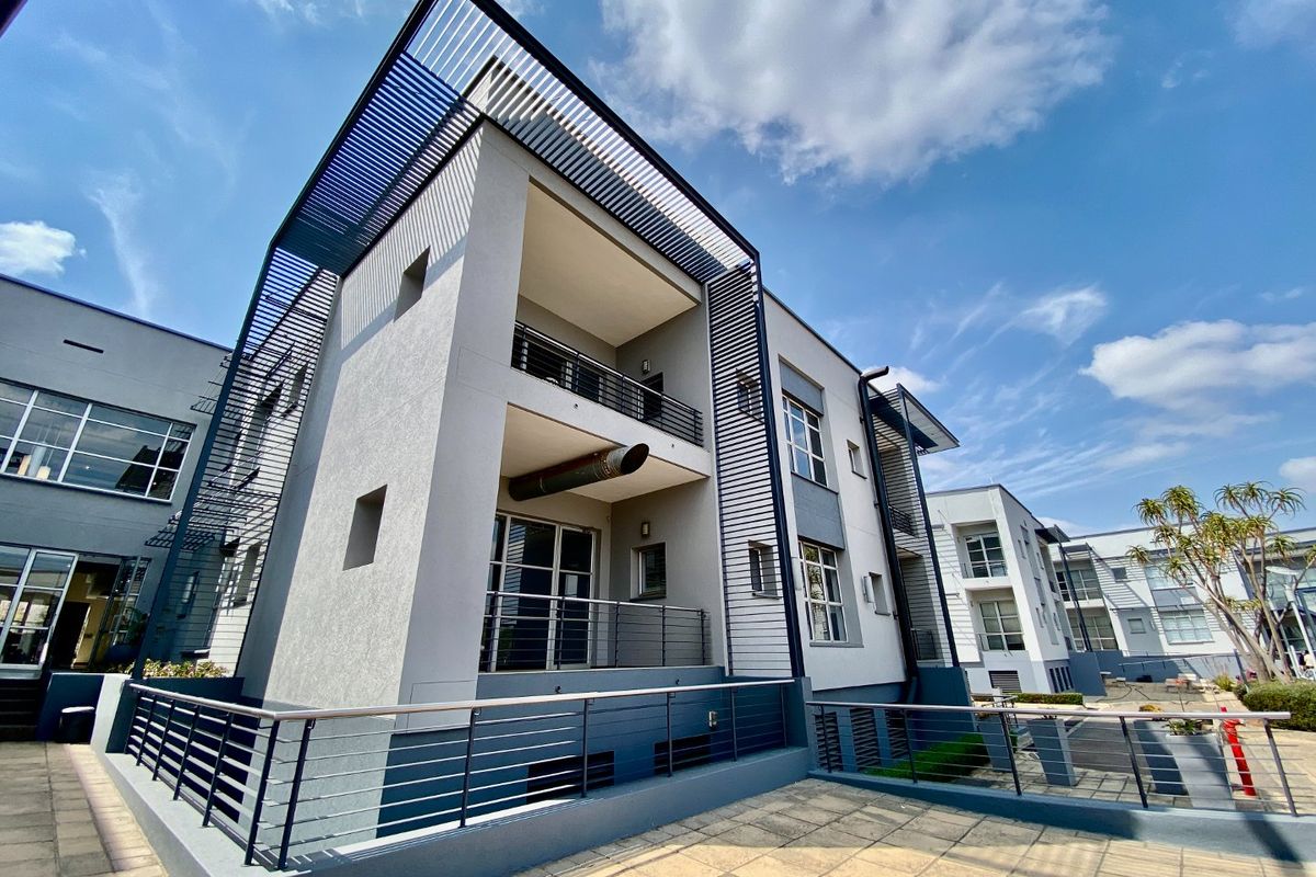 Modern commercial building exterior featuring multi-level balconies, metal architectural detailing, and a paved terrace area.