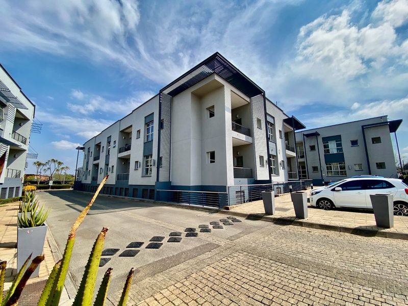 A modern multi-story commercial building exterior featuring a paved driveway, balconies with metal railings, and a clean, contemporary facade design.