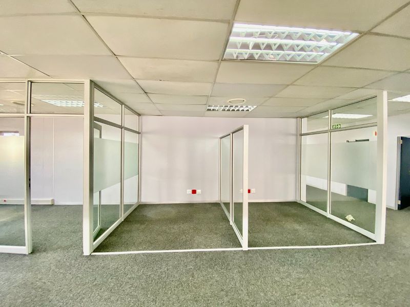 Open-plan commercial office space featuring glass partition walls, suspended ceilings with recessed lighting, and carpeted flooring.
