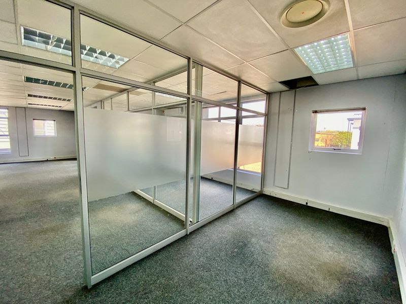 Empty commercial office space featuring glass partition walls, suspended ceilings with recessed lighting, and carpeted flooring, suitable for a professional workspace layout.