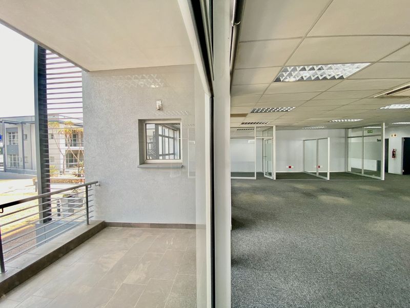 Spacious open-plan commercial office area featuring a suspended ceiling, glass partitioning, and direct access to a private balcony with tiled flooring.