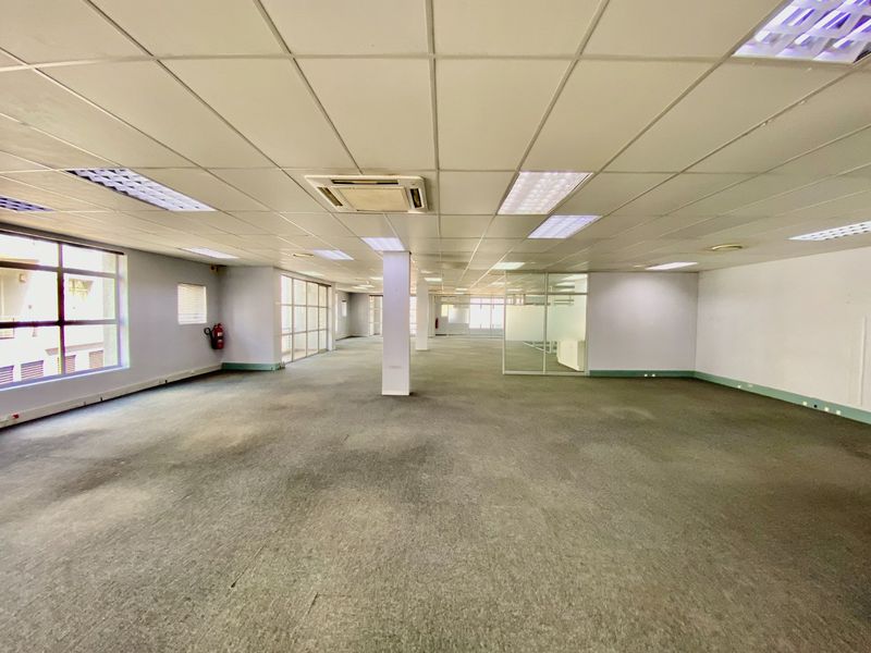 Spacious open-plan commercial office area featuring suspended ceilings, recessed lighting, central air conditioning, and large windows providing ample natural light.