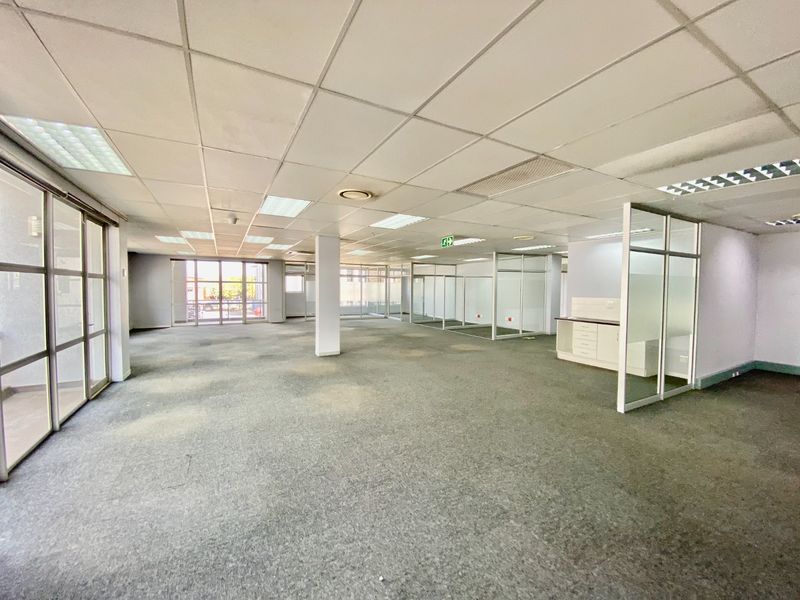 Spacious open-plan commercial office space featuring glass partitions, suspended ceilings with recessed lighting, and a small built-in kitchenette area.