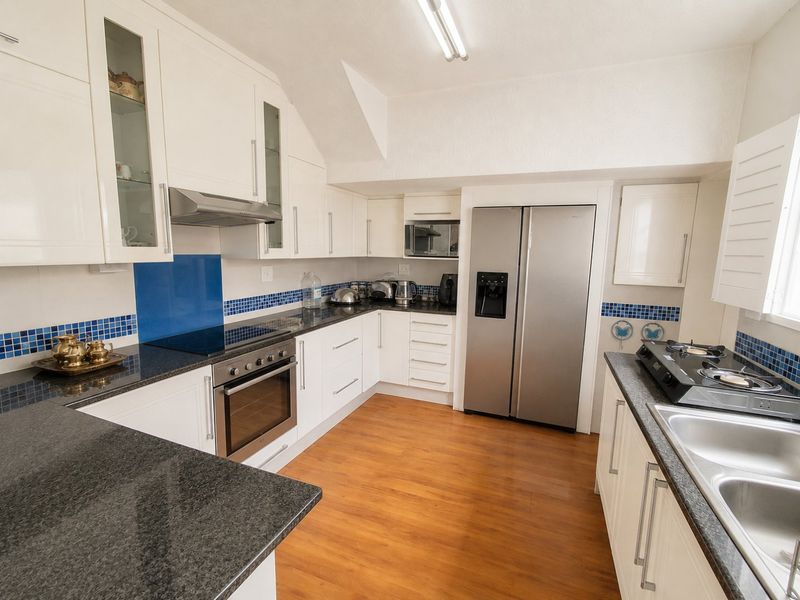 A well-appointed kitchen featuring white shaker-style cabinetry, dark granite countertops, integrated appliances, and a blue tiled backsplash.